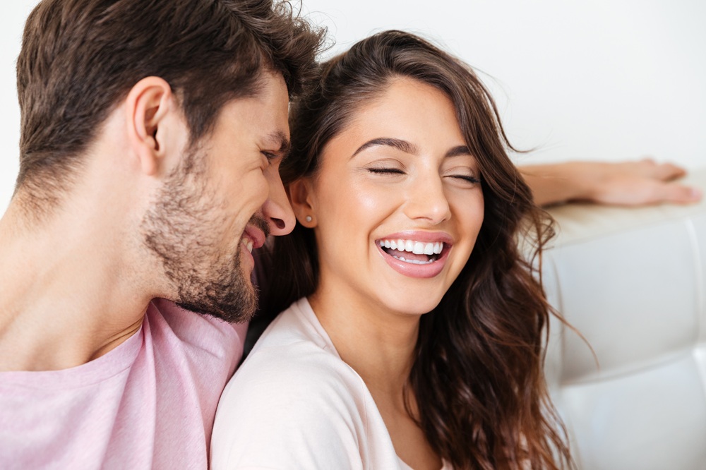 A happy couple relaxing on a couch, with the woman laughing and showing her bright smile – Dentist East Village