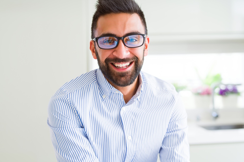 A cheerful man in a striped shirt and glasses smiling in a bright, modern kitchen – Dentist East Village