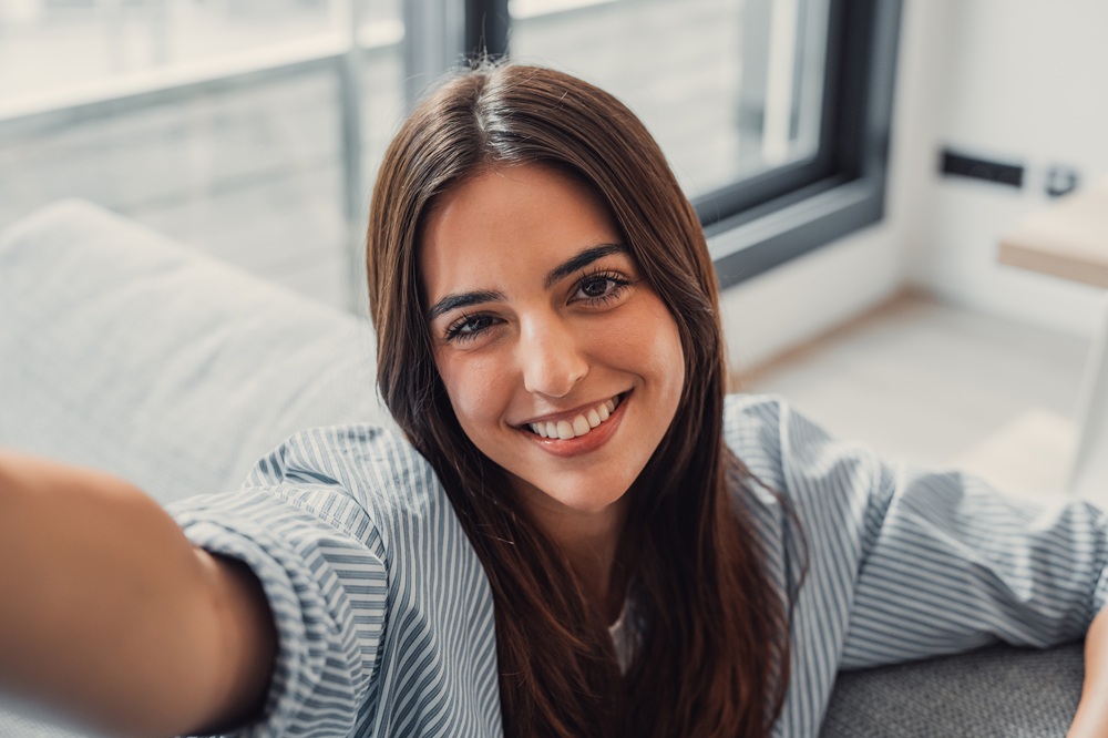 A woman with long brown hair and a striped shirt smiles brightly while taking a selfie indoors – Dentist by Union Square