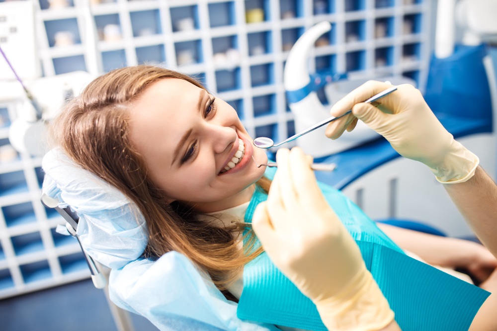 Patient Smiling During Dental Exam – Union Square Oral Surgery A woman reclines in a dental chair, smiling as a dentist wearing gloves holds examination tools – Union Square Oral Surgery